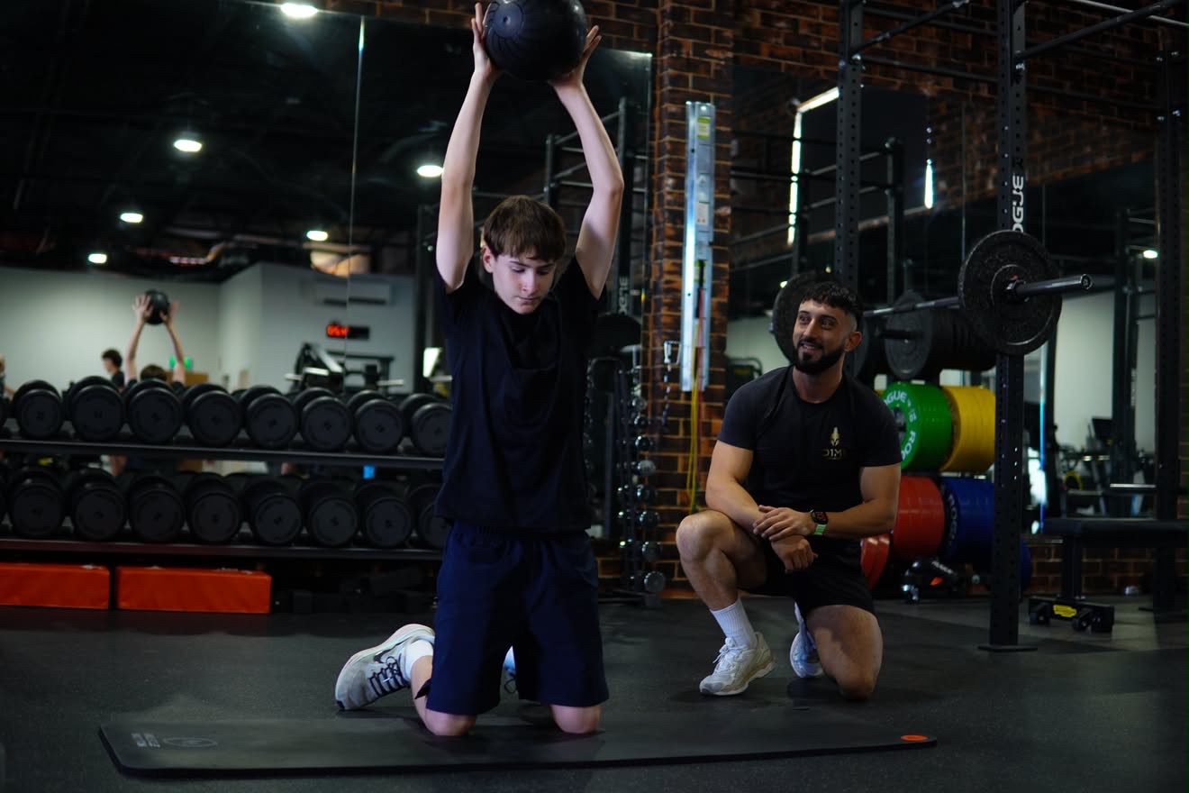 Athlete pressing a medicine ball overhead during a coached session on the D1M1 gym floor